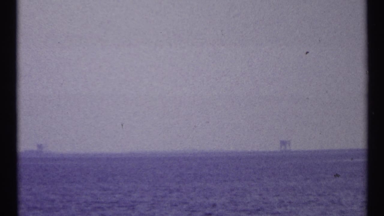 Purple-tinted 8mm view of open water near Toronto, with faint horizon structures and film gate edges visible.