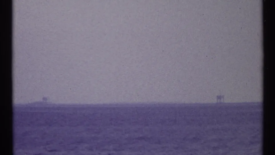 Hazy 1967 waterfront frame with open water in the foreground and small distant forms along the horizon.