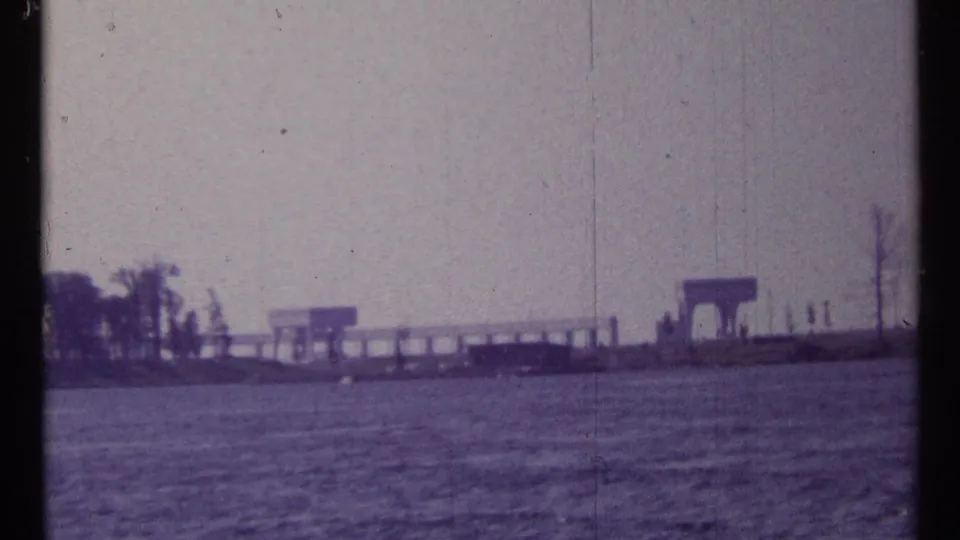 1967 Toronto waterfront view showing a shoreline pier, trees, water, and a small structure in soft 8mm haze.
