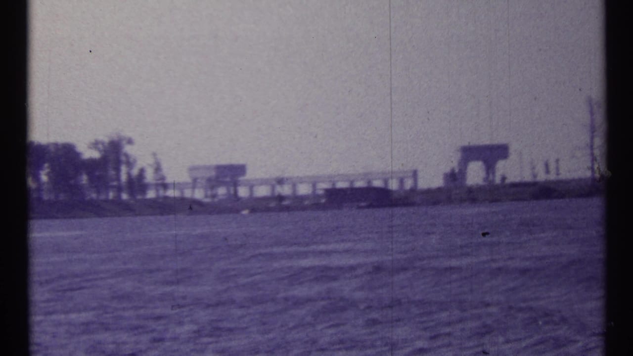 Distant shoreline and industrial structures across open water under a hazy sky.