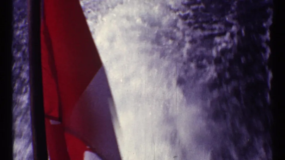 Close 8mm view from the boat with a red-and-white flag and bright rushing water filling much of the frame.