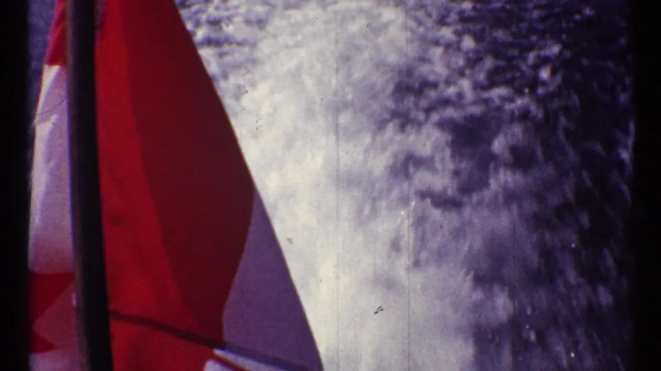 Final 1967 8mm frame shows the boat flag and foamy wake or spray, with heavy grain and handheld framing.