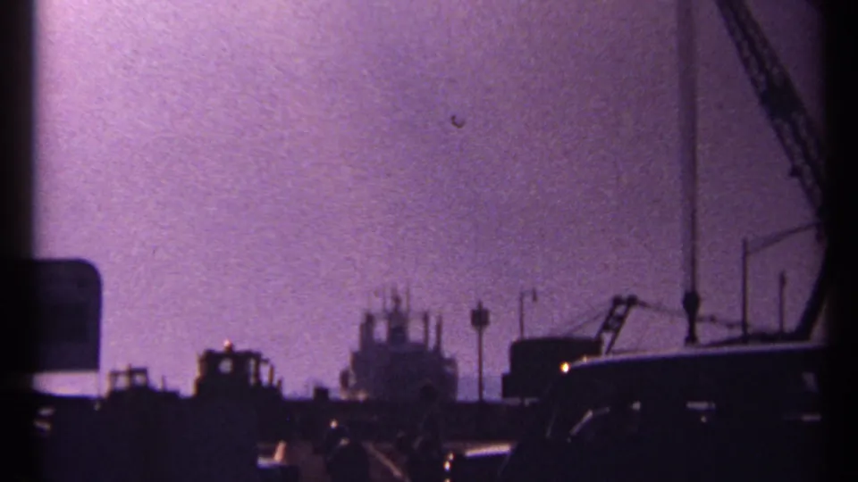 Low-light 1967 Toronto harbor view with silhouetted cranes, vehicles, dock structures, and grainy purple 8mm exposure.