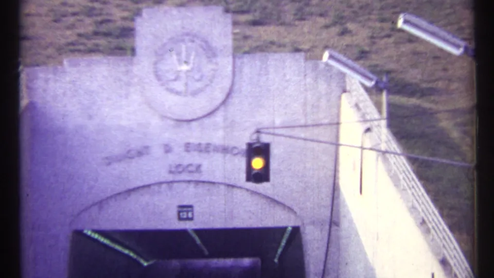 1967 8mm frame of the Dwight D. Eisenhower Lock entrance with emblem, sign, traffic light, and railings.