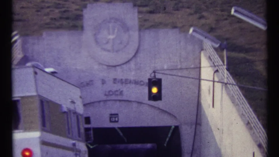 1967 8mm frame showing a white truck approaching the Eisenhower Lock entrance under a yellow traffic signal.