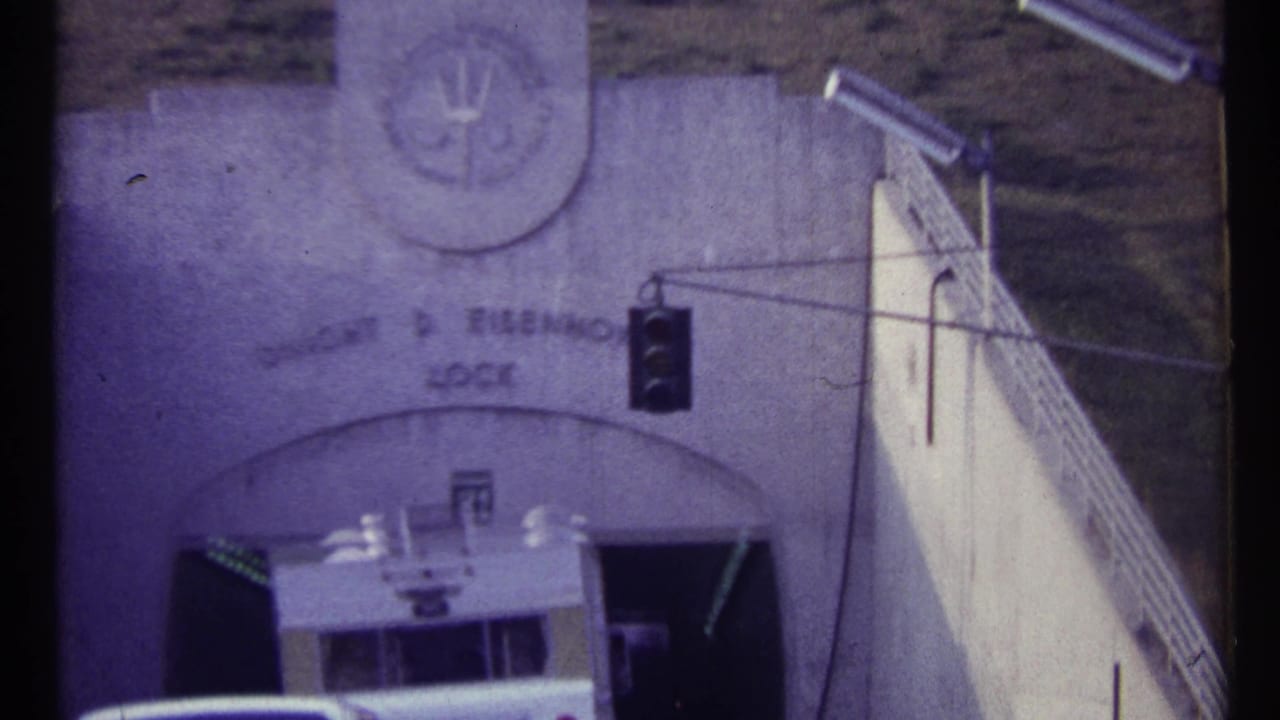 White vehicle approaching a concrete tunnel entrance beneath a traffic light.