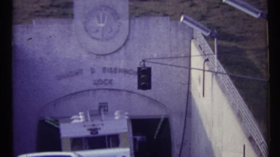 1967 Canadian 8mm frame showing a white vehicle near a concrete tunnel portal with a dark traffic signal and wall marking above.