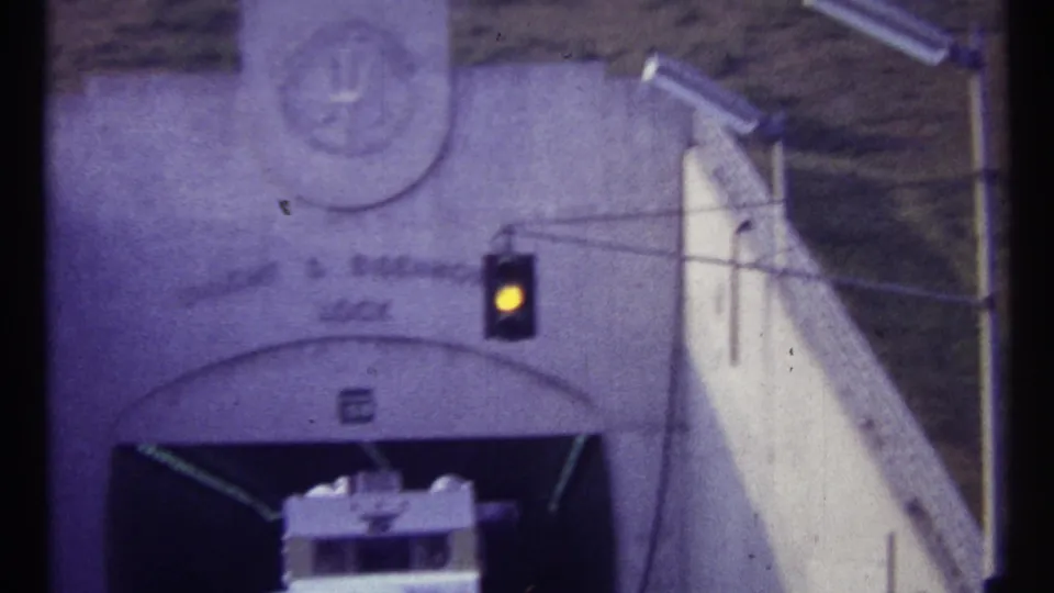 1967 Canadian 8mm frame with an amber signal lit above a white vehicle entering or waiting at a concrete hydroelectric station portal.