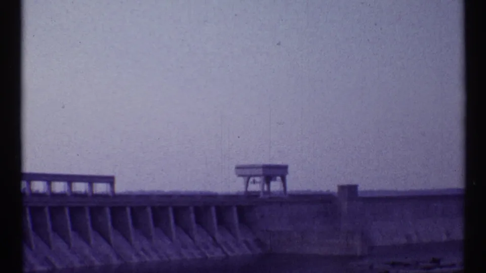 1967 Toronto home-movie frame showing a cropped dam section with angled concrete supports and a small top platform.
