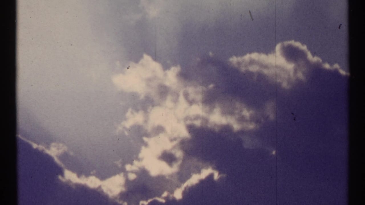 Bright clouds and sunlit haze against a deep blue sky on faded 8mm film.