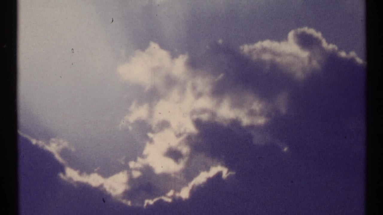 1967 Toronto sky shot with layered clouds, bright cloud edges, blue-purple color shift, and small physical-film marks.