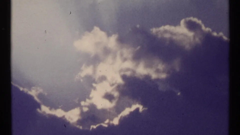 1967 Toronto sky shot with layered clouds, bright cloud edges, blue-purple color shift, and small physical-film marks.