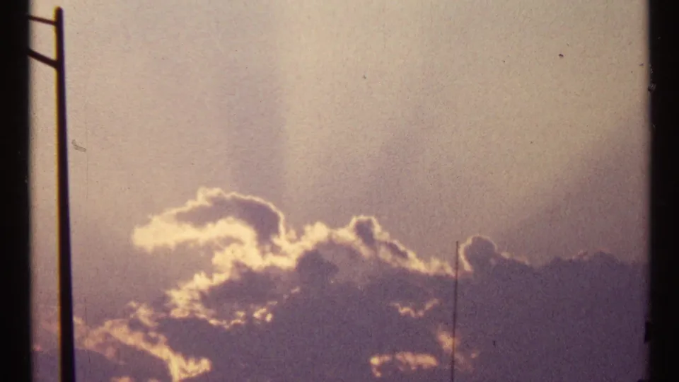 Warm 1967 home-movie sunset view with golden light outlining clouds over an urban setting.