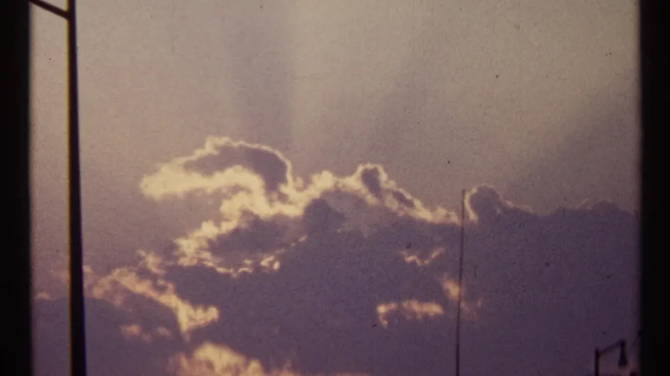 1967 Toronto sunset footage showing backlit clouds, warm sky color, film grain, and a partial streetlight below.