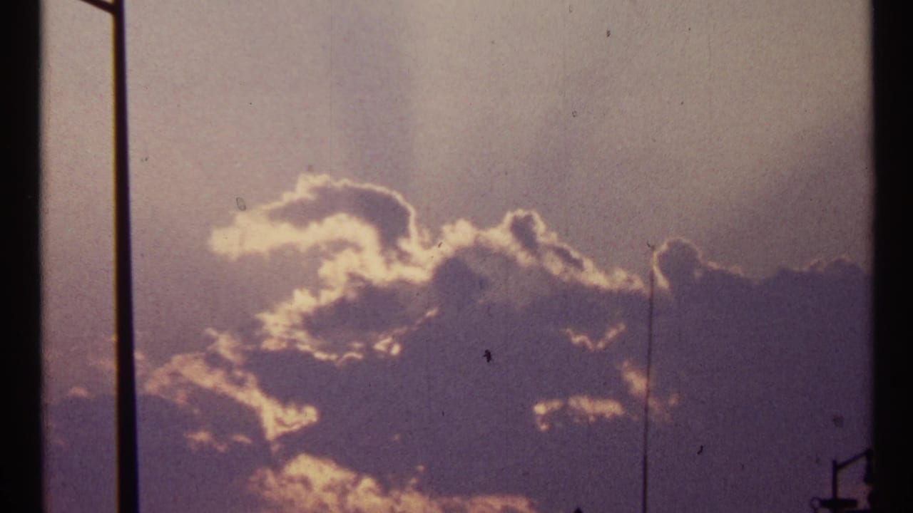 Backlit clouds fill the sky, crossed by dark vertical bars and a small lamp silhouette.