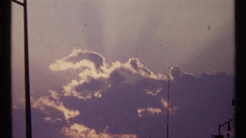 1967 Toronto 8mm view of a bright cloud bank, vertical dark bars, and a small waterfront lamp silhouette near the edge.