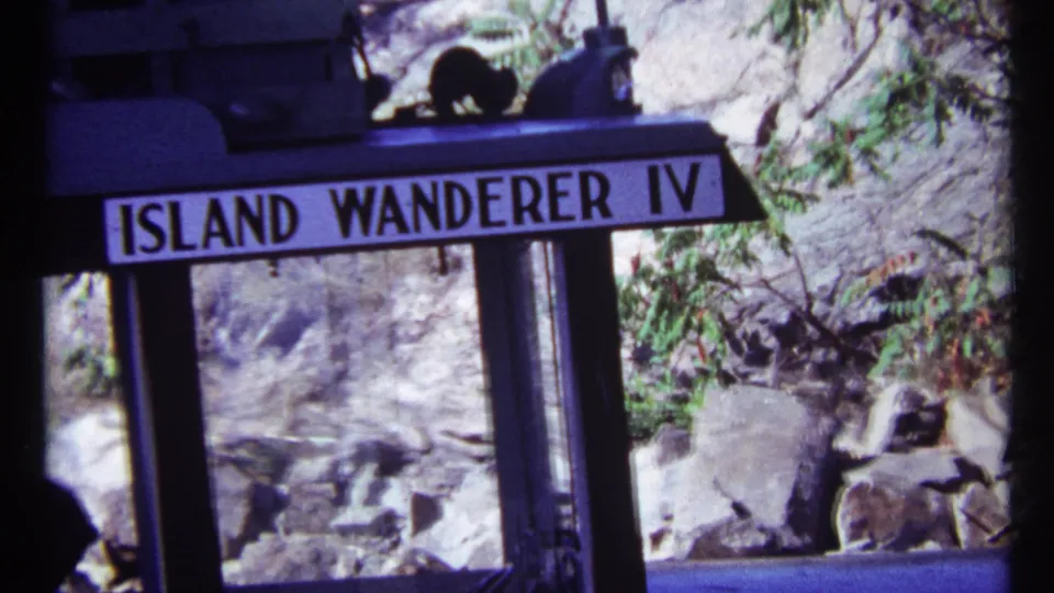 A closer 8mm view of the Island Wanderer IV sign shows the boat window frame, shoreline rocks, and trees in Toronto in 1967.