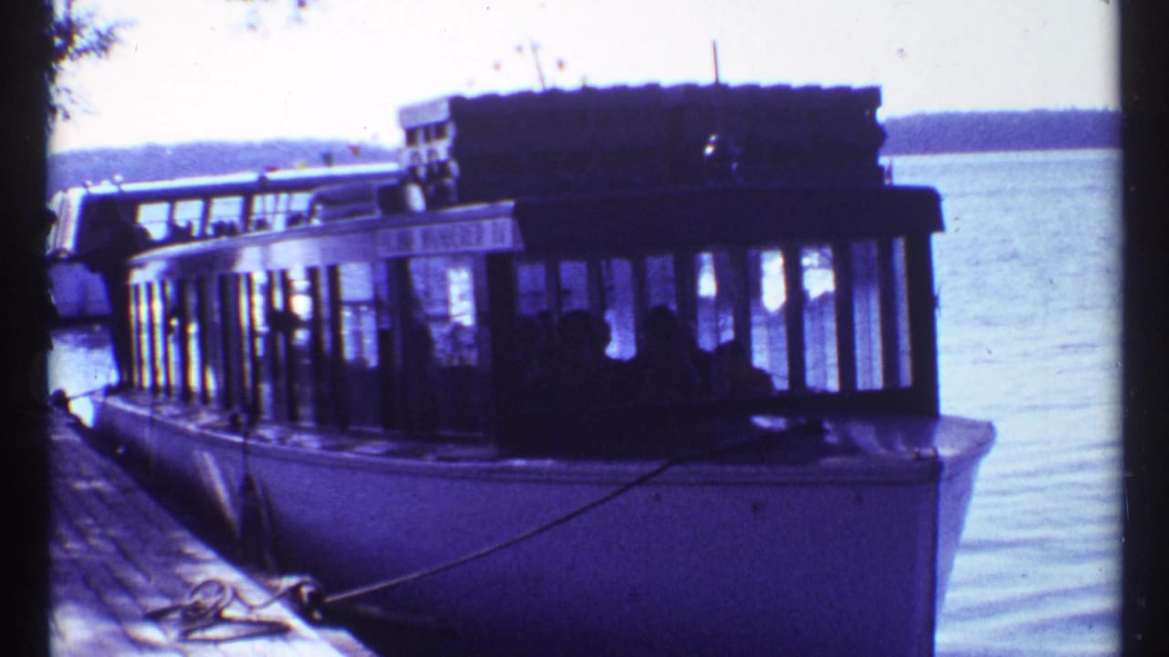 Passenger boat tied near the dock with another boat moving across the water behind it.
