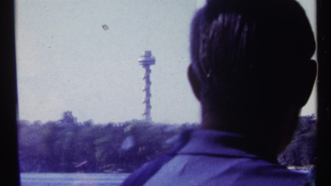 Silhouetted man at a boat window with water, trees, and a distant tower beyond.