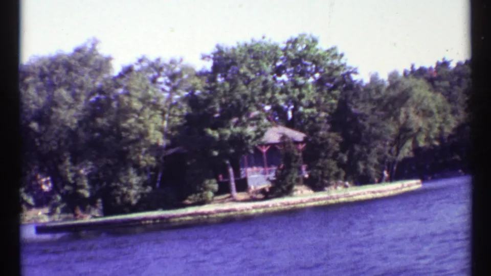 Final 1967 8mm frame shows the wooded island or shoreline receding, with a small cabin-like structure beside blue lake water near Toronto, Canada.