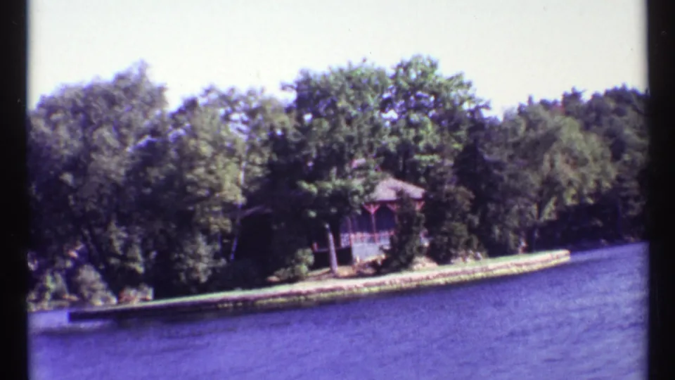 1967 Toronto home-movie view from a boat toward a tree-lined shoreline with a small gazebo-like structure by the water.