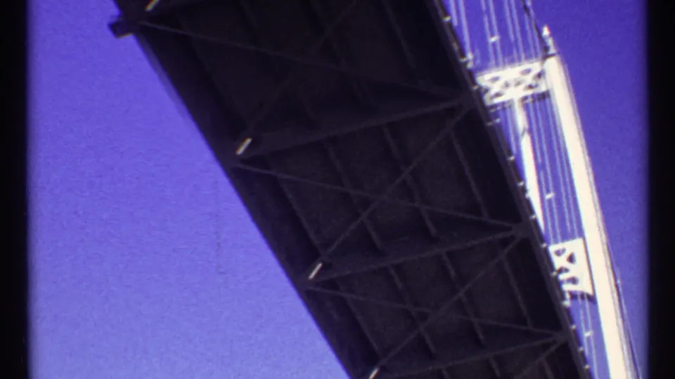 Low-angle 1967 Toronto boat perspective under a high bridge, with dark underside framing white tower sections and cables.