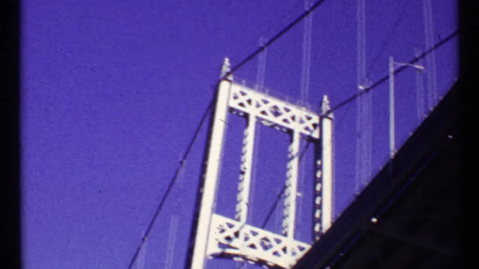1967 Toronto 8mm frame showing a white suspension bridge tower, latticework, and cables against saturated sky.