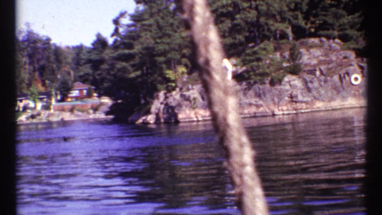 Calm lake beside a rocky wooded shoreline with a small distant structure.