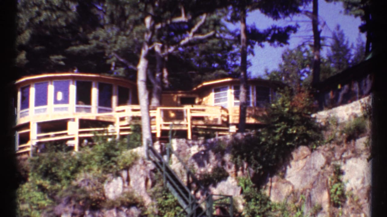 Modernist lakeside house with curved balcony on a rocky wooded cliff.