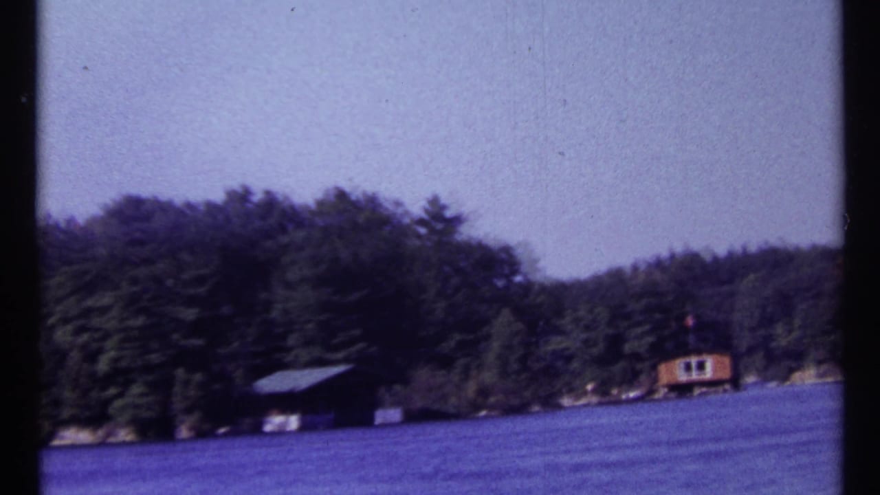 Wooded lake shoreline with a small cabin at the right edge and dark frame divider.