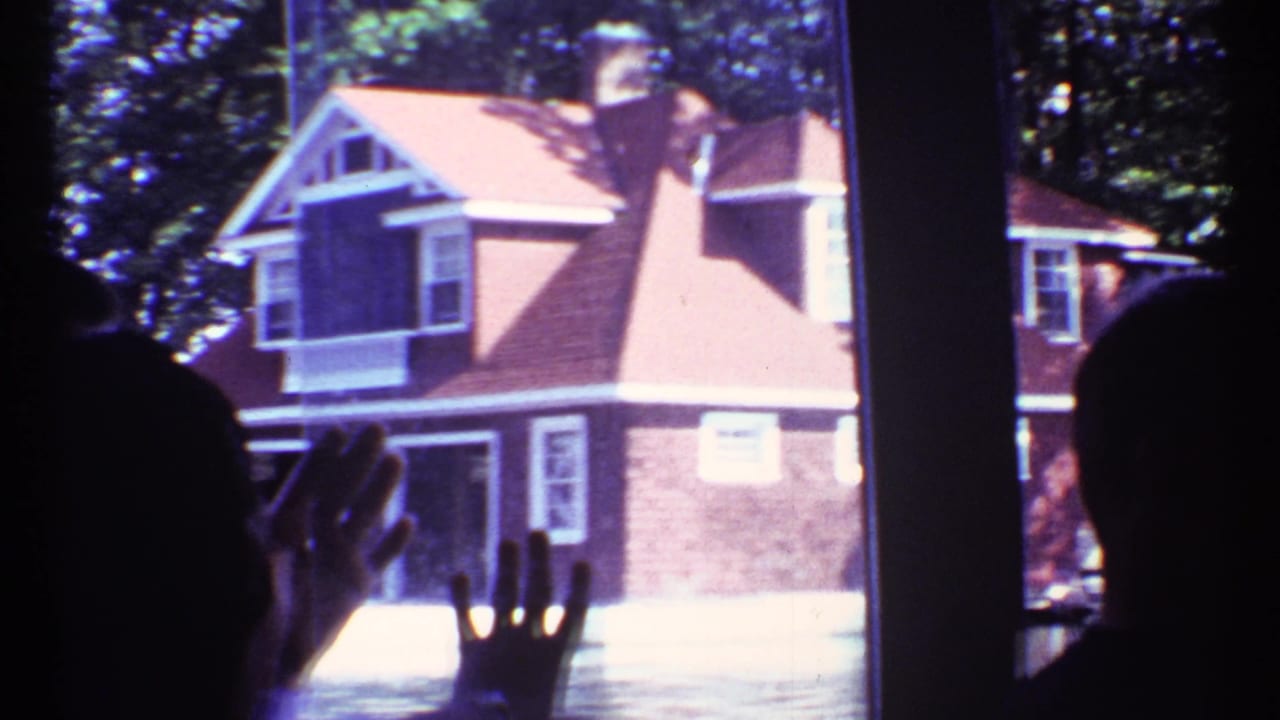 Interior silhouettes frame a 1967 Toronto view of a red-sided house with white trim seen through large window panes.