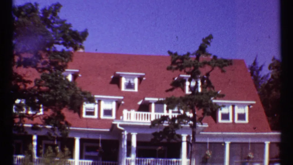 Late frame of the 1967 Toronto house tour showing the red-roofed home, white porch details, dormers, and trees across the front.