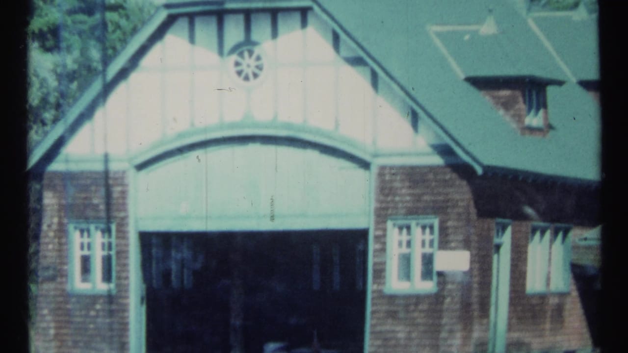 Brick boathouse with pale arched entrance, green roof, and small windows.