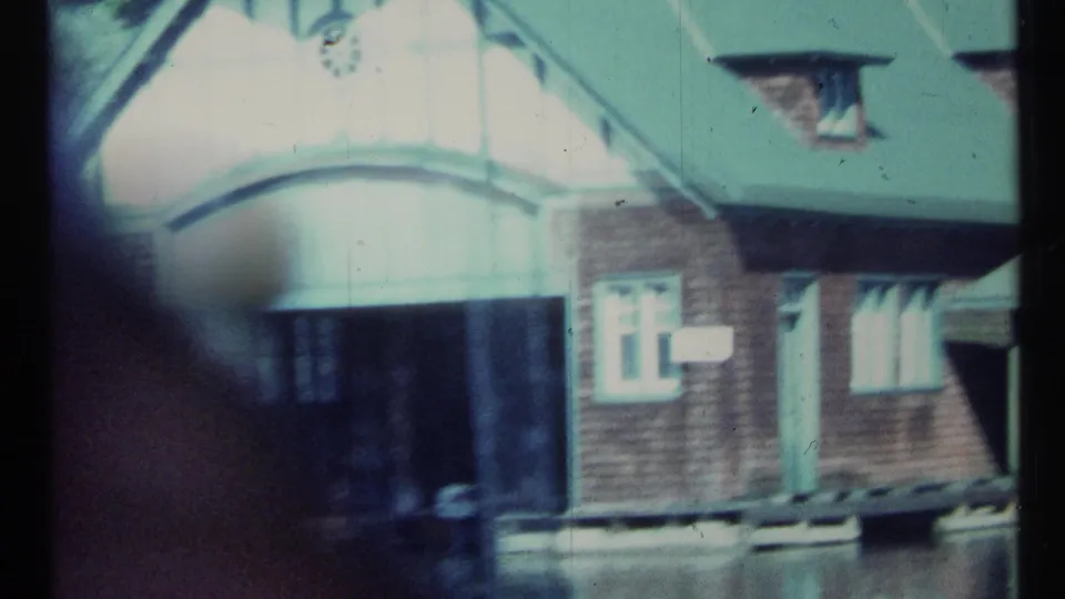 Closer 1967 Toronto frame of the lakeside boathouse facade, showing the pale arched entrance, brick walls, green roof, and dock edge.