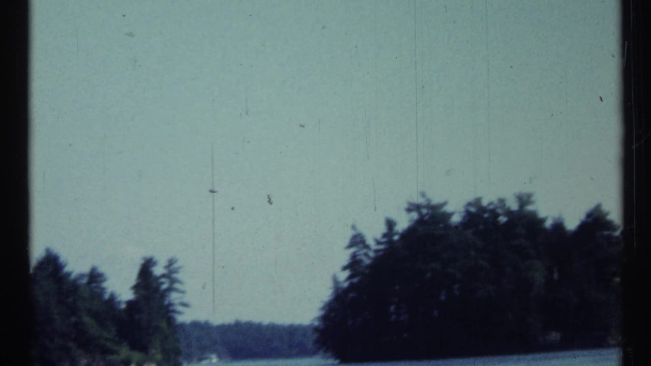 Forested shoreline and pale sky seen through a dark film frame edge.
