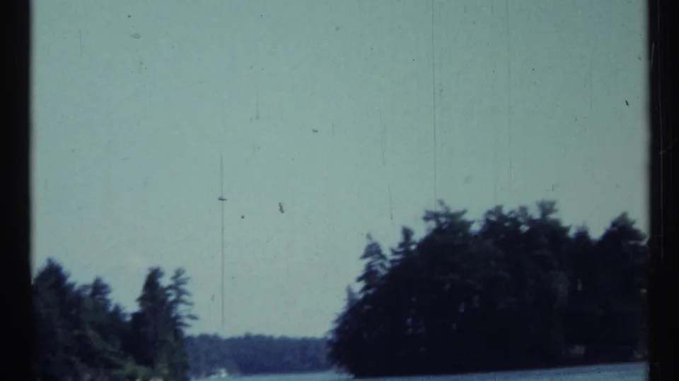 1967 Toronto-area 8mm frame showing a distant wooded shoreline under pale sky, with film scratches and gate edges visible.