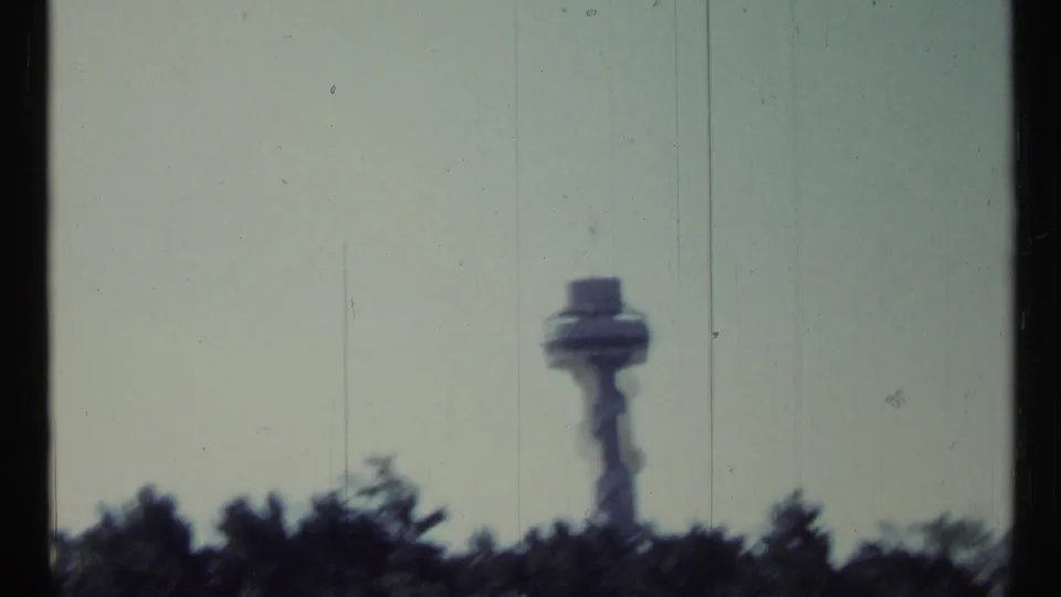Soft 8mm view of a distant Toronto control tower above wooded foreground, with muted color and visible film wear.