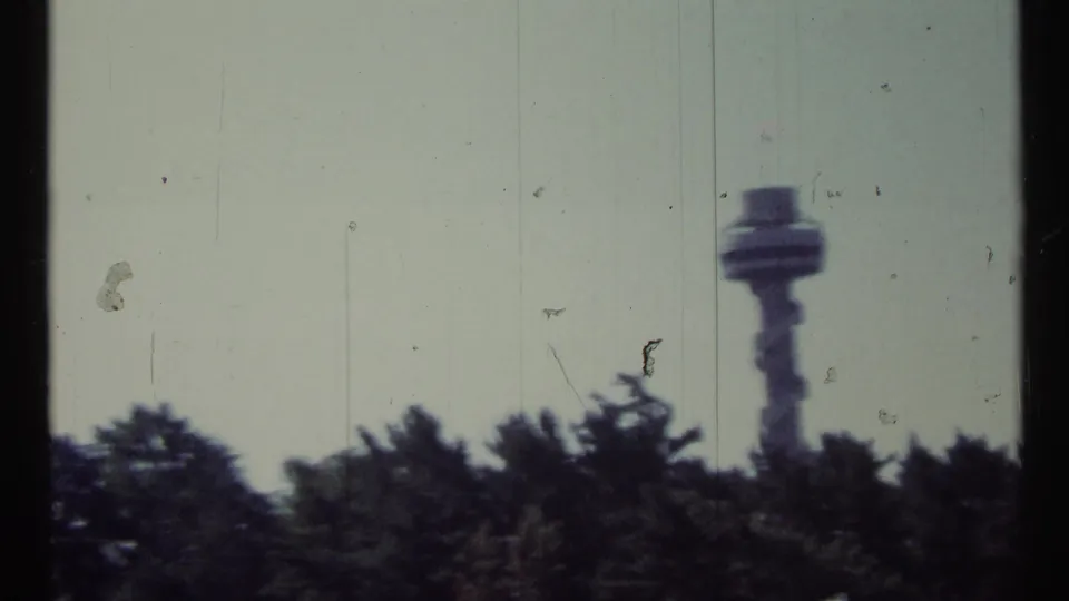 1967 Toronto-area frame showing the control tower at right, rising beyond treetops in a worn 8mm home-movie scan.