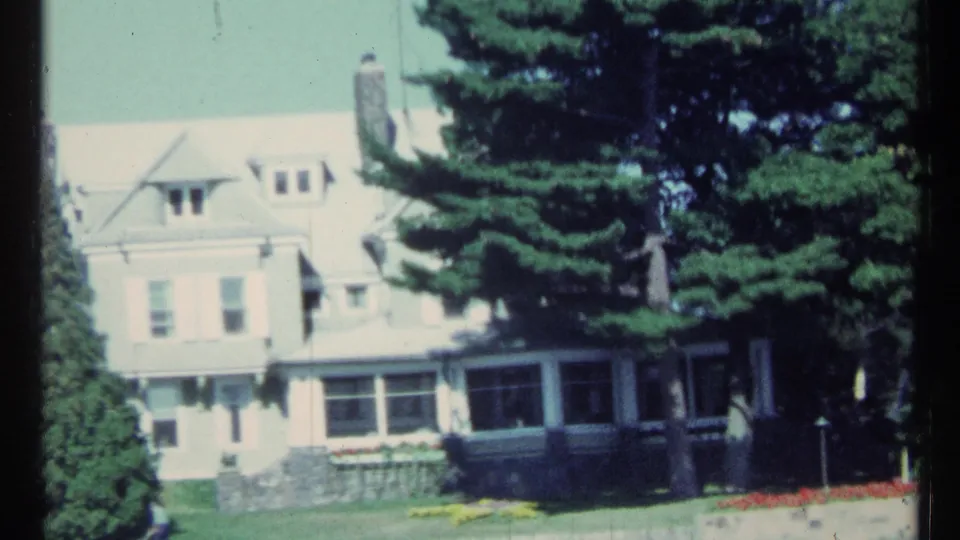 1967 Toronto home-movie frame showing a large pale mansion-like house partly screened by tall trees and garden plantings.