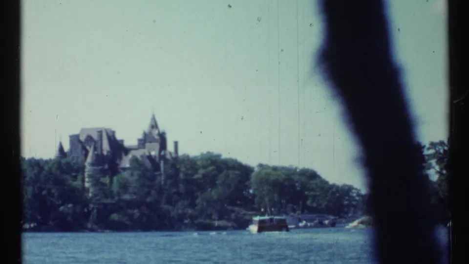 1967 Toronto waterfront frame with a distant castle-like building, trees along the shore, boats, and dark foreground obstruction.