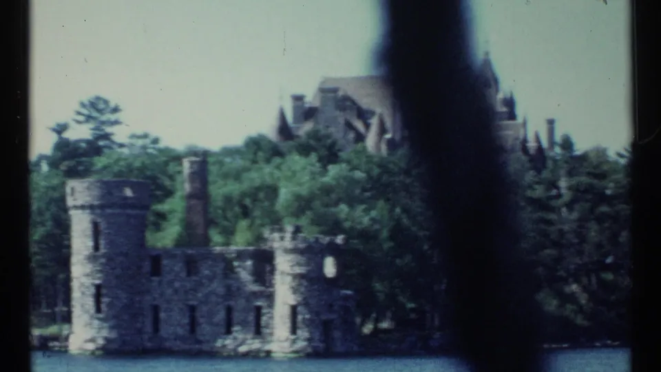 Stone ruins on the waterline appear below a wooded slope and large castle-like mansion in this 1967 Toronto home-movie frame.