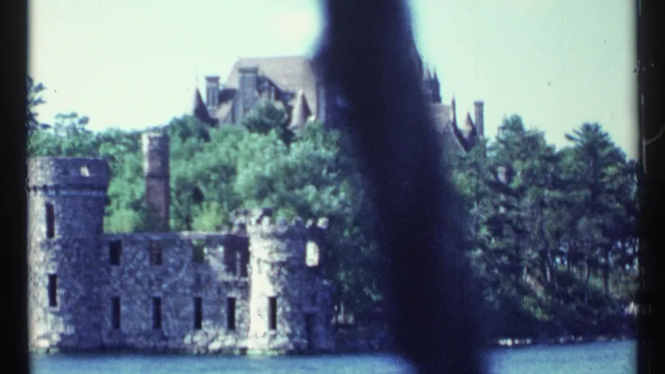 The final frame holds on stone ruins at the water's edge, trees, and a partly visible mansion, with a dark shape crossing the 8mm frame.