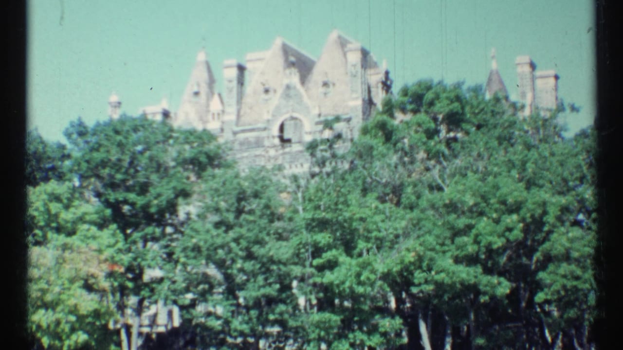 Turreted stone building rising above dense green trees.