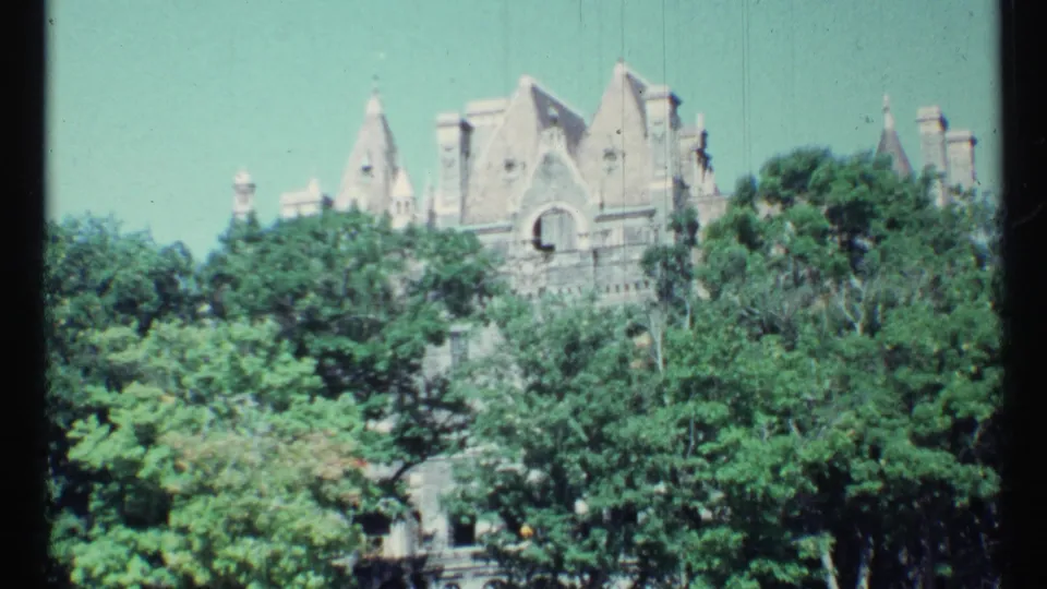 1967 Toronto 8mm view of a large castle-like stone building with steep roofs, partly screened by trees.