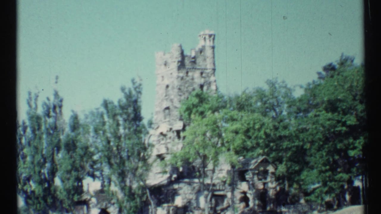 Stone castle tower rising above leafy trees under a clear sky.