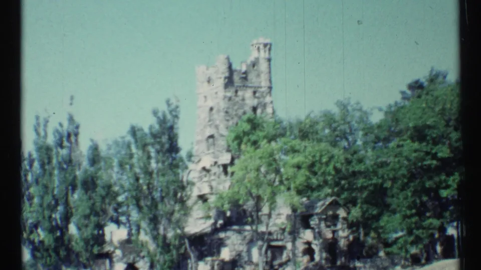 1967 Toronto home-movie frame showing a pale stone castle-like tower partly hidden by summer trees.