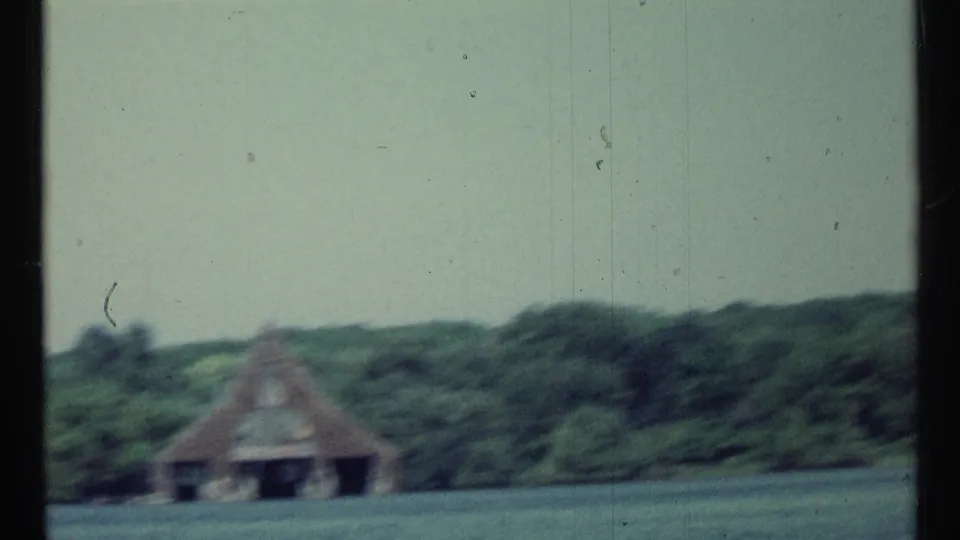 Soft 1967 Toronto lake view with a boathouse and trees seen from across the water during a pan.