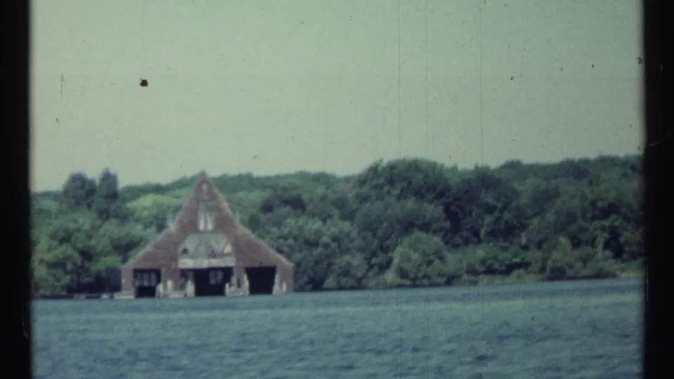 1967 Toronto 8mm frame with rippled lake water in front of a boathouse and tower-like shoreline structure.