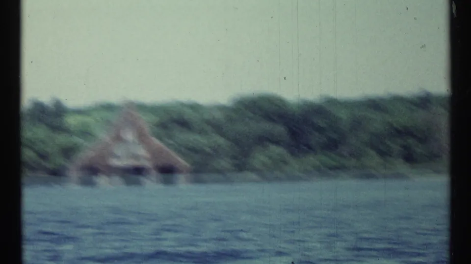 Blurred 1967 Toronto 8mm view of the lakeside boathouse and wooded shore near the end of the pan.
