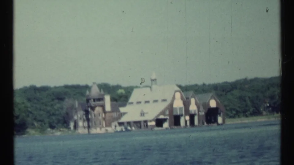 Boat-view frame of a distinctive lakeside estate with arched boathouse-like openings and wooded background in 1967 Toronto-area footage.